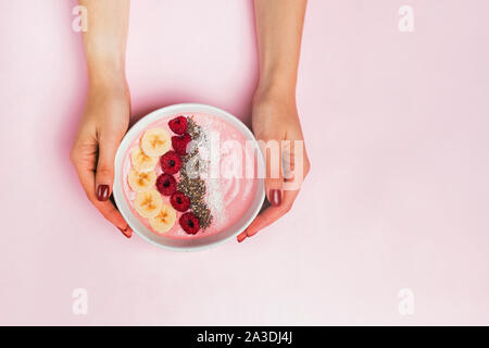 Woman's hands holding smoothie bowl with raspberries on pink background Stock Photo