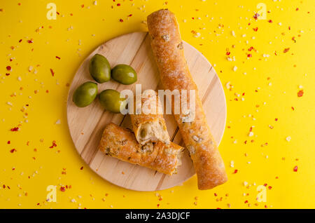 Italian olive bread on wooden cutting board on yellow background. Top view with copy space Stock Photo
