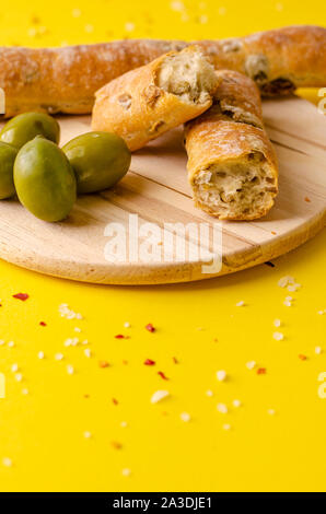 Italian olive bread on wooden cutting board on yellow background. Vertical with copy space Stock Photo