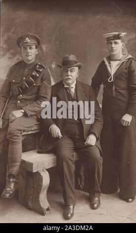 Vintage Early 20th Century Photographic Postcard Showing a Father With His Two Sons. One a British Army Soldier From The Royal Artillery. The Other Son a British Navy Sailor From H.M.S.Valient. Stock Photo