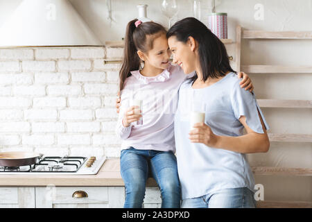Mother and daughter drinking milk in kitchen and touching foreheads Stock Photo
