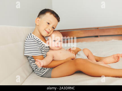 Cute little six month old baby girl and his older brother, playing at home in bed in bedroom, smiling happily Stock Photo
