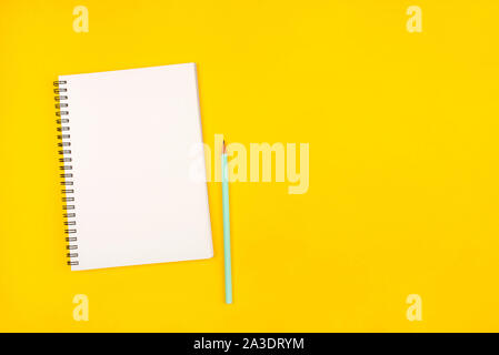 Empty notebook and pencil on yellow background, top view. Stock Photo
