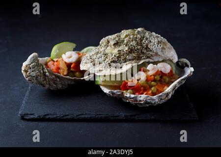 Oyster shell with seafood salad and lime on dark background Stock Photo