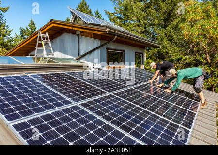 Workers install solar photovoltaic panels on a homeowners roof in British Columbia, Canada. Stock Photo