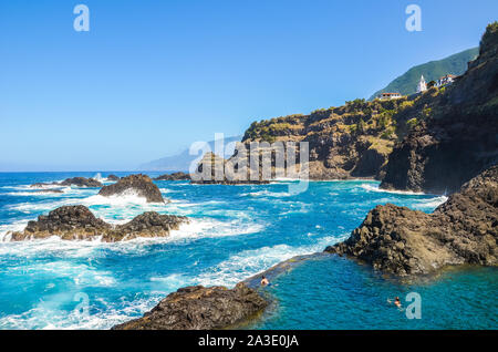 Seixal, Madeira, Portugal - Sep 13, 2019: People swimming in natural swimming pools in the Atlantic ocean. Pools made up of volcanic rock, into which the sea flows naturally. Tourist attraction. Stock Photo