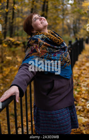 Fat girl on the bridge around maple leaves and autumn forest at sunset Stock Photo