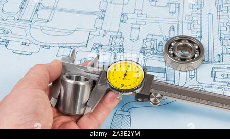 Steel part measurement by caliper in human hand. Ball bearing on technical drawing of combustion engine. Quality control. Engineer with precise tool. Stock Photo