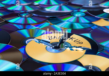 Damaged compact disc. Secure backup and disposal of digital personal data. Broken optical storage device on green-blue texture. Old archiving media. Stock Photo