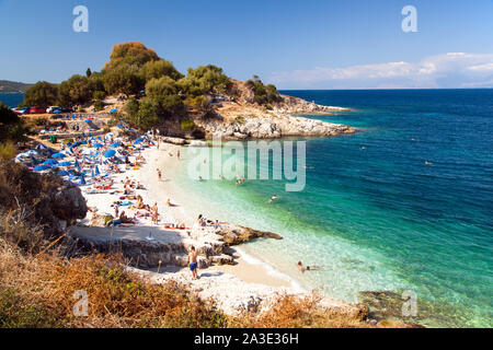 Holidaymakers sunbathing on sunbeds and loungers under parasols on the beach at the Greek holiday resort of Kassiopi on the Island of Corfu Greece Stock Photo