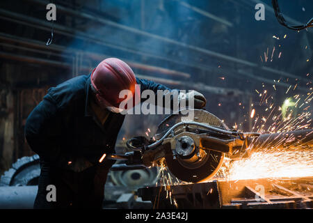 Employee grinding steel with sparks - focus on grinder. Steel factory. Stock Photo