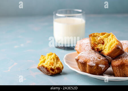 Homemade muffins with dried apricots sprinkled with powdered sugar and a glass of milk on a light blue background, horizontal orientation, copy space Stock Photo