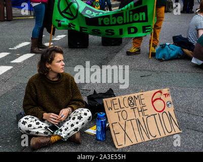 London, UK. 7th October 2019. A protester sits in Broad Sanctuary with a poster 'Welcome to the 6th Extinction'.Extinction Rebellion begin the International Rebellion by occupying eleven locations at government ministries, Downing St, The Mall, Westminster and Lambeth bridges, bringing traffic to a halt. They demand the government tell the truth about the climate and ecological emergency, act to halt biodiversity loss, reduced emissions to net zero and create and be led by a Citizens Assembly. Peter Marshall/Alamy Live News