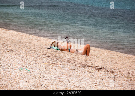 Woman lying on a shingle beach reading a kindle book reader Stock Photo