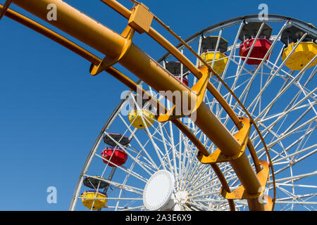 Ferris wheel with red and yellow passenger cabins above a yellow roller coaster track under a perfect blue sky Stock Photo