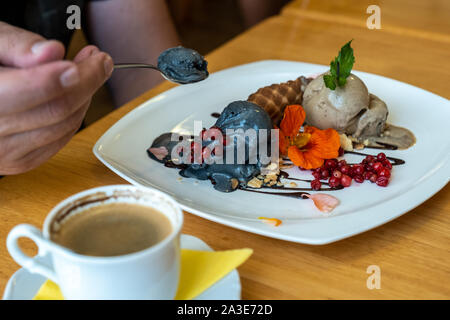 A man eats coal and chicory ice cream, decorated with waffles and fresh berries. Stock Photo