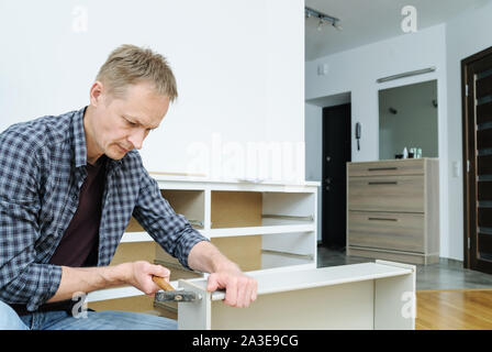 Mounting the chest of drawers. The  man is using a hammer to fix the drawer's boards. Stock Photo
