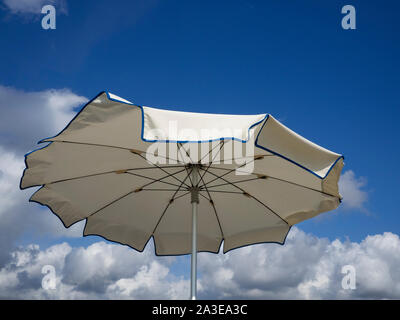 white beach umbrella viewed from above sways moved by the sea breeze . Blue sky with  white clouds background, copy space Stock Photo