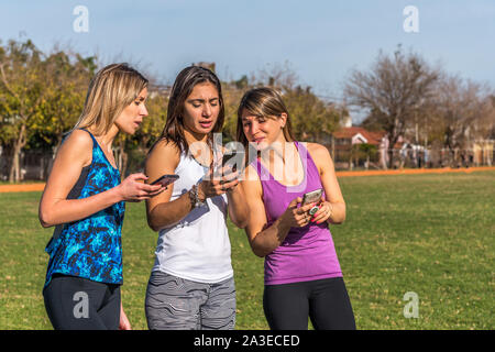 Happy friends in the park on a sunny day . Lifestyle portrait of three women friends enjoy nice day with their smartphones.
