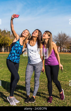 Happy friends in the park on a sunny day . Lifestyle portrait of three women friends enjoy nice day with their smartphones. Stock Photo
