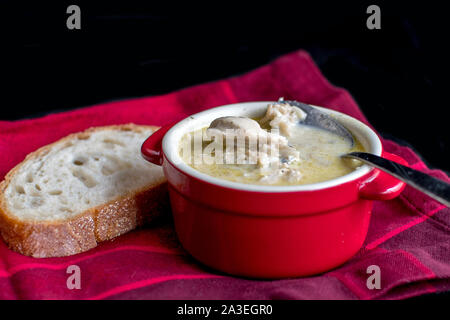 A crock of creamy chicken and rice soup, and a slice of chewy bread, sit on a red cloth napkin Stock Photo