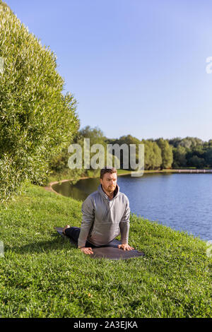 Inspired man doing yoga asanas in city park. Fitness outdoors and life balance concept. Stock Photo
