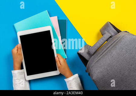 Back to school, education, learning concept. Top view to kid hands with tablet computer, notebooks, books and backpack on colorful background Stock Photo