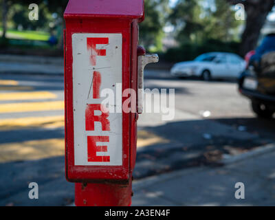 Outdoor fire alarm call box at urban intersection, fire in bold font Stock Photo