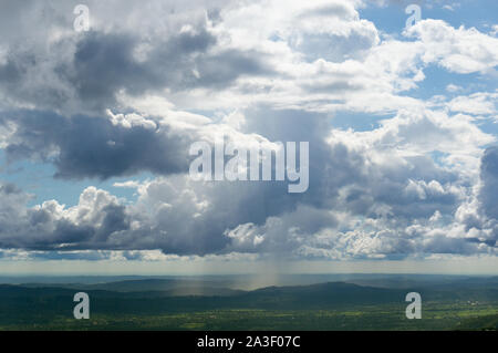 Dramatic beautiful sky with clouds and blue patches in between over a hilly green terrain Stock Photo