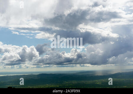 Dramatic beautiful sky with clouds and blue patches in between over a hilly green terrain Stock Photo