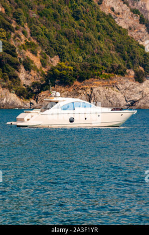 White luxury sea boat floating near the rocky coastline with green mountains on the background in Monterosso Al Mare, Cinque Terre, Italy Stock Photo