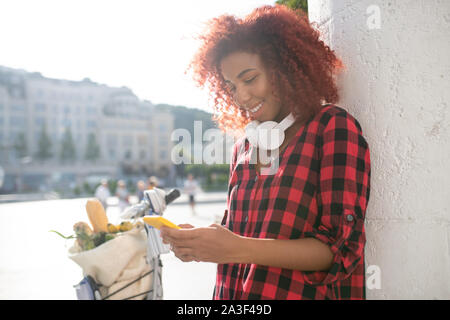 Woman with earphones on neck reading message from friend Stock Photo