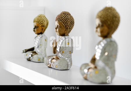 Three small decorative Buddha figurines on shelf in the room in a row Stock Photo