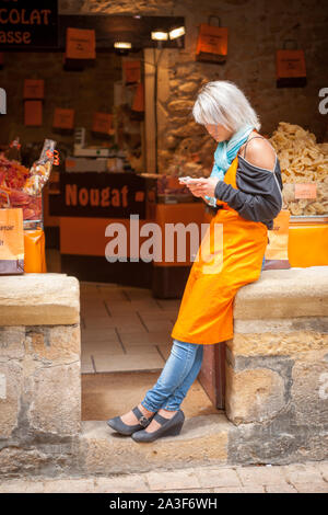 Young woman shop keeper texting on her phone in front of her open shop Stock Photo