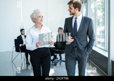 Senior mature caucasian female executive ceo discuss report with young colleague, serious old aged mentor reads paper explains business plan to employ Stock Photo