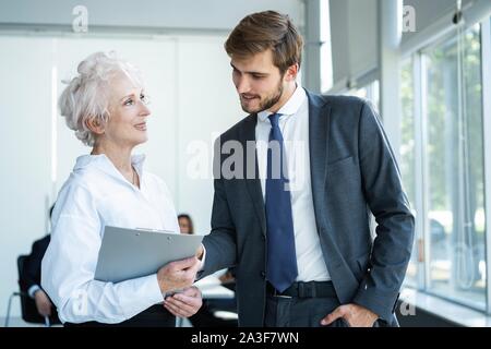 Senior mature caucasian female executive ceo discuss report with young colleague, serious old aged mentor reads paper explains business plan to employ Stock Photo