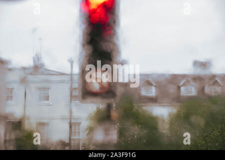 A set of traffic lights set on red as seen through a heavily rain covered car windscreen obscuring the view of the town beyond. Stock Photo