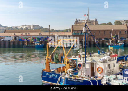 The harbour at Scarborough. Two fishing boats moored to a quayside with a busy wharf in background. Hotels and hill are in the distance. Stock Photo