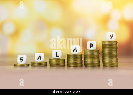 Payroll and salaries ladder increase growth money coins on table and success concept / salary text block with stacked coins on bokeh background Stock Photo