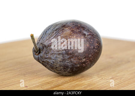 One whole rotten purple plum with bamboo plate isolated on white background Stock Photo