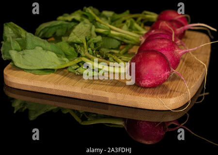 Group of five halves of fresh red radish on bamboo cutting board isolated on black glass Stock Photo