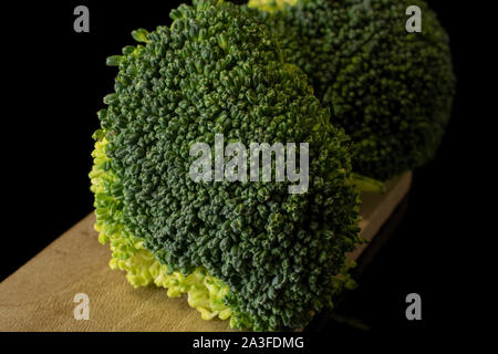 Group of two whole fresh green broccoli on  wooden board isolated on black glass Stock Photo