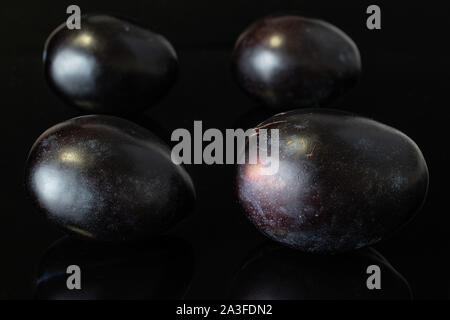 Group of four whole fresh purple plum isolated on black glass Stock Photo