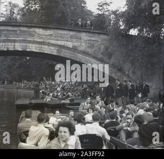 1953, historical, large numbers of students and teachers from the colleges of Cambridge Unversity gather together on punts by a bridge on the river Cam. Stock Photo