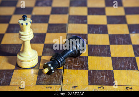 defeated black king lying at the feet of the white king on the chessboard closeup Stock Photo
