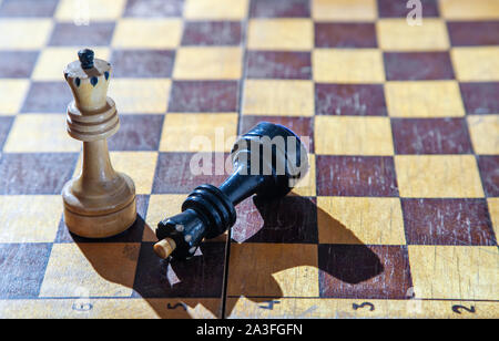 defeated black king lying at the feet of the white king on the chessboard closeup Stock Photo