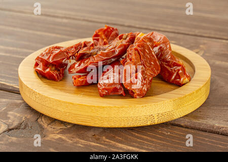 Lot of slices of dry red cherry tomato on bamboo plate on brown wood Stock Photo