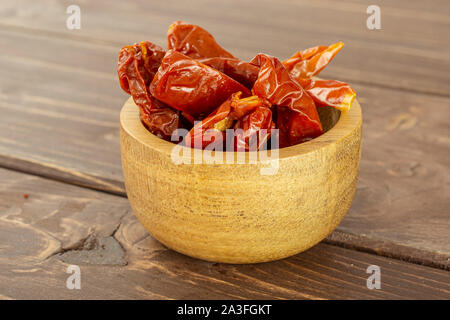 Lot of slices of dry red cherry tomato in wooden bowl on brown wood Stock Photo