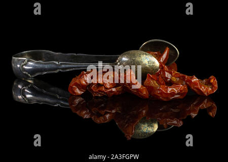Lot of slices of dry red cherry tomato with sugar tongs isolated on black glass Stock Photo