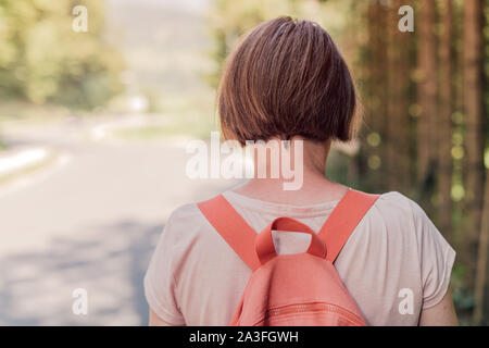 Female hiker walking by the road through countryside, rear view of woman hiking down the roadway on sunny summer day